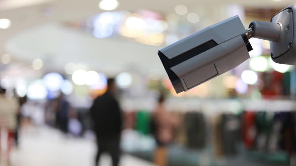 White commercial CCTV camera looking out inside a commercial mall or similar complex as part of a business CCTV security system.