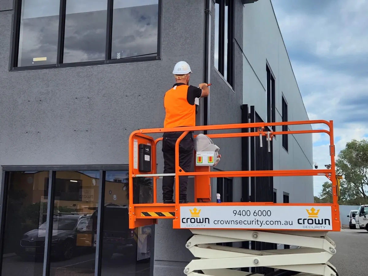 Crown Security technician installing a security system on a commercial building exterior using an elevated work platform